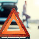 A young man with a silver car that broke down on the road.He has set up a warning triangle.He is waiting for the technician to arrive.